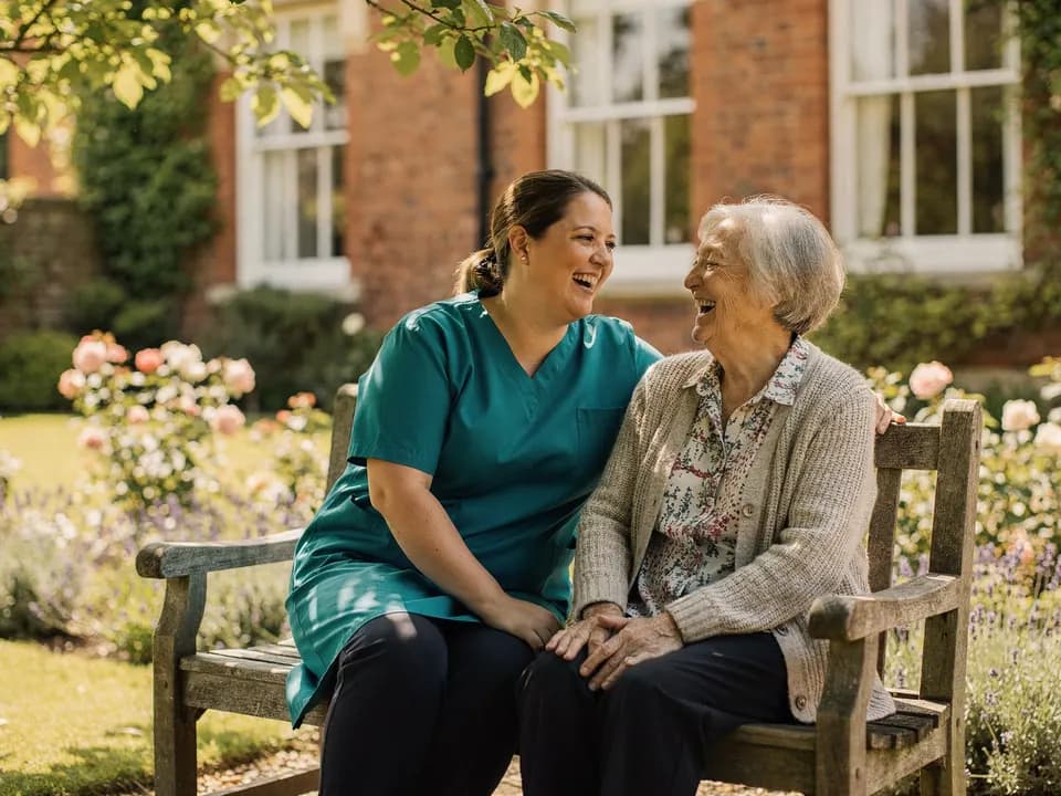 A care worker and a resident laughing together on a garden bench